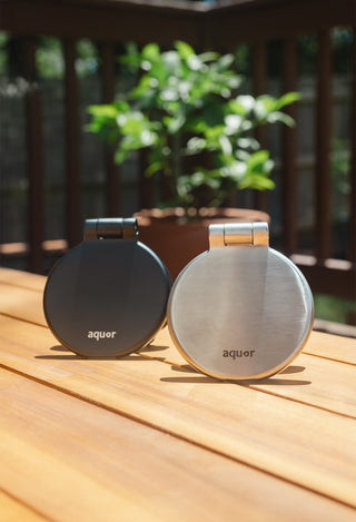 From left to right, a matte black v1+ debris cover and a brushed stainless v1+ debris cover sitting on a deck. 