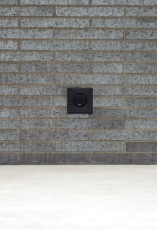 A matte black house hydrant v1+ installed on brick with a black mounting box.