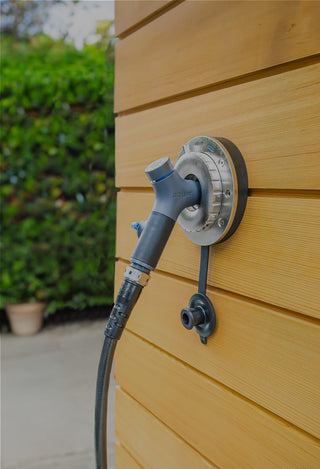 Aquor hot+cold hydrant installed onto the wooden siding of a home with a comfort grip vb hose connector and hose plugged in.